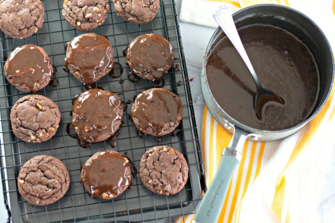 Drizzling chocolate frosting over cookies on a wire cooling rack