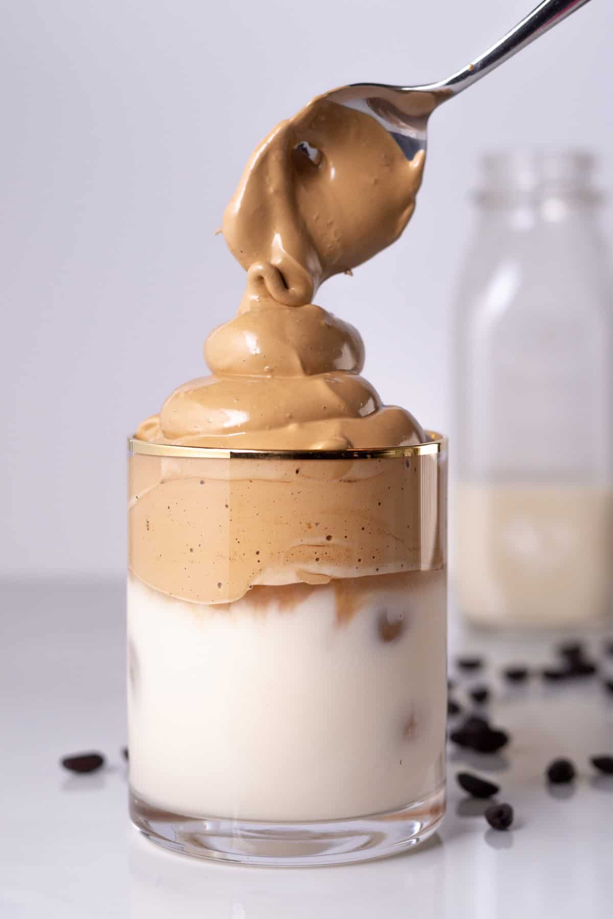 Dalgona coffee, also called "whipped coffee," is known for its light and airy top layer that resembles a coffee flavored fluffy whipped cream. adding whipped dalgona coffee mixture on top of milk using a spoon