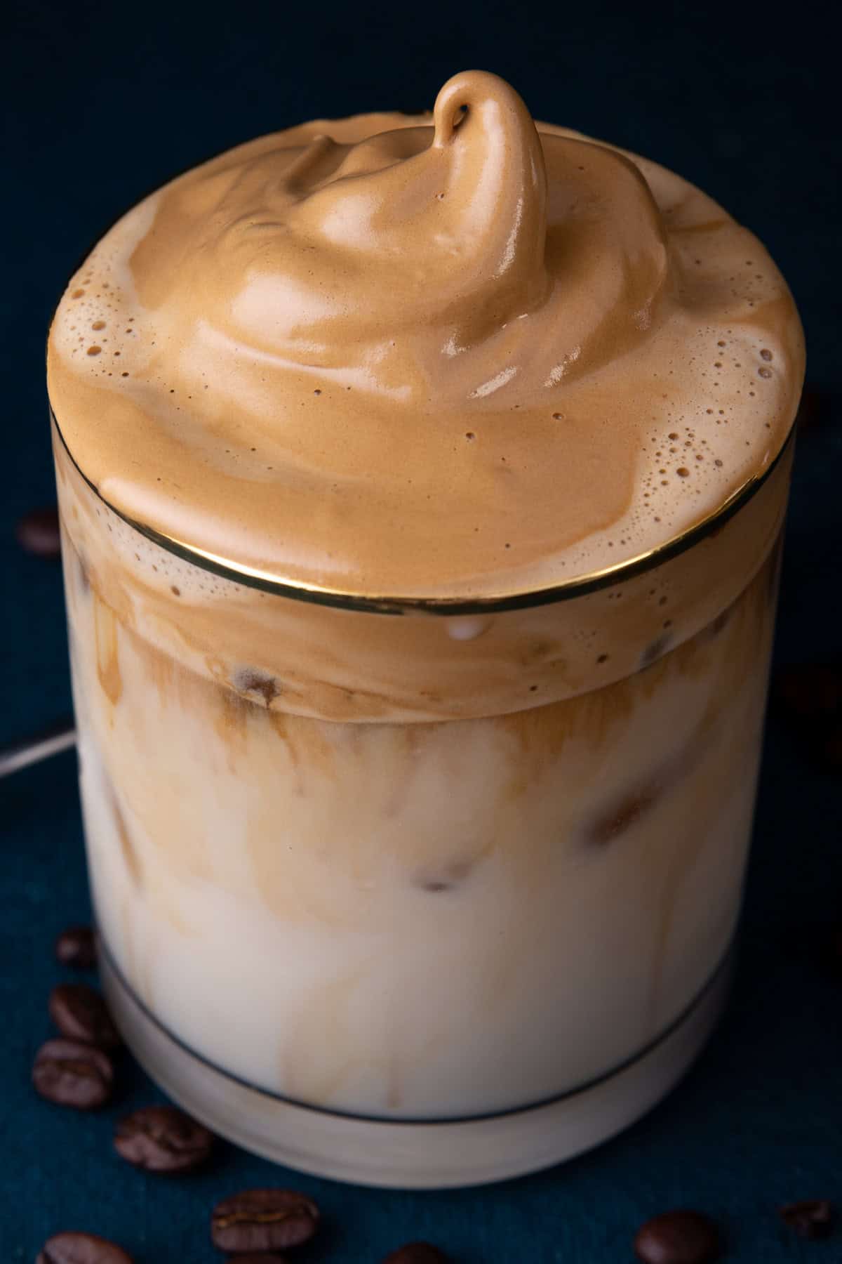 Dalgona coffee, also called "whipped coffee," is known for its light and airy top layer that resembles a coffee flavored fluffy whipped cream. top view of whipped Dalgona iced coffee