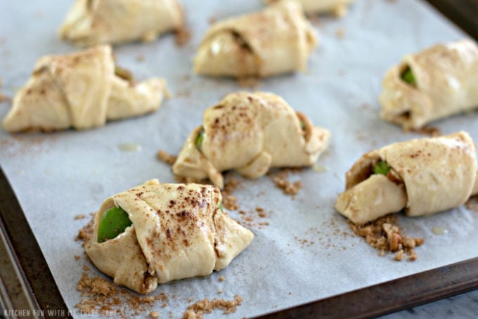 apples rolled into crescent rolls on a parchment paper lined baking sheet