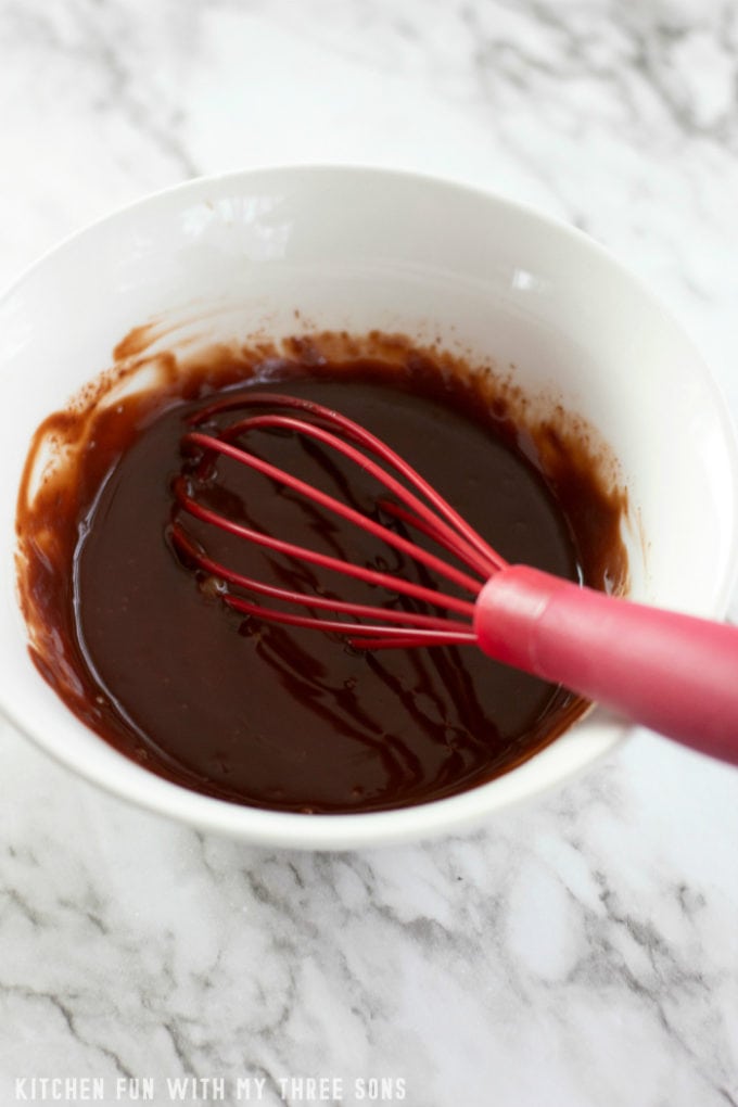 whisking homemade chocolate ganache in a white bowl with a red whisk