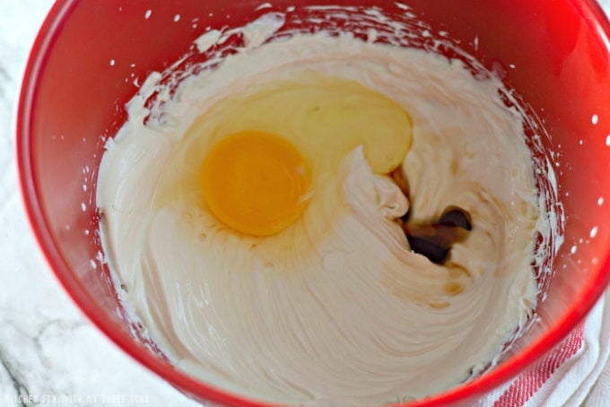 mixing egg, vanilla, sugar, and cream cheese together in a red mixing bowl