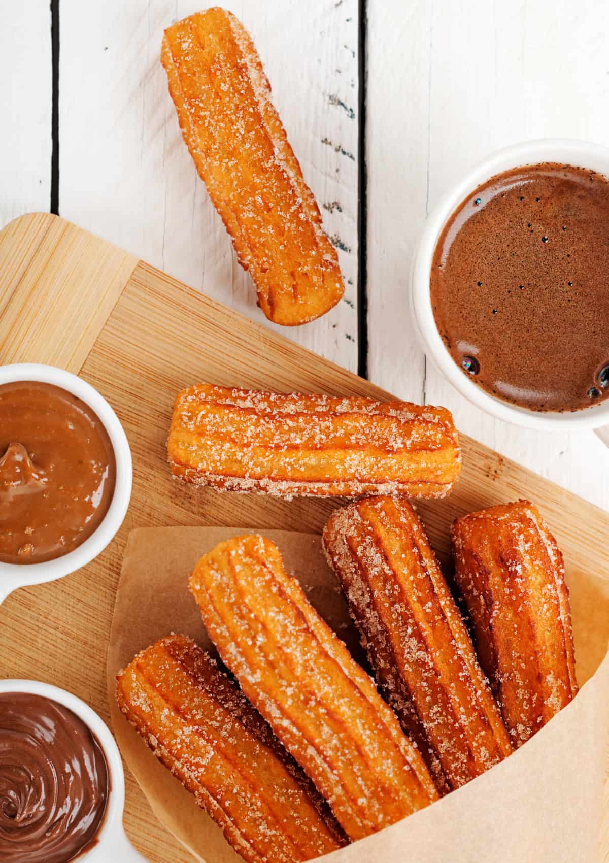 These Churros are soft on the inside, crisp and golden brown on the outside, and tossed with cinnamon sugar. Overhead view of churros on the counter with three cups of dipping sauce
