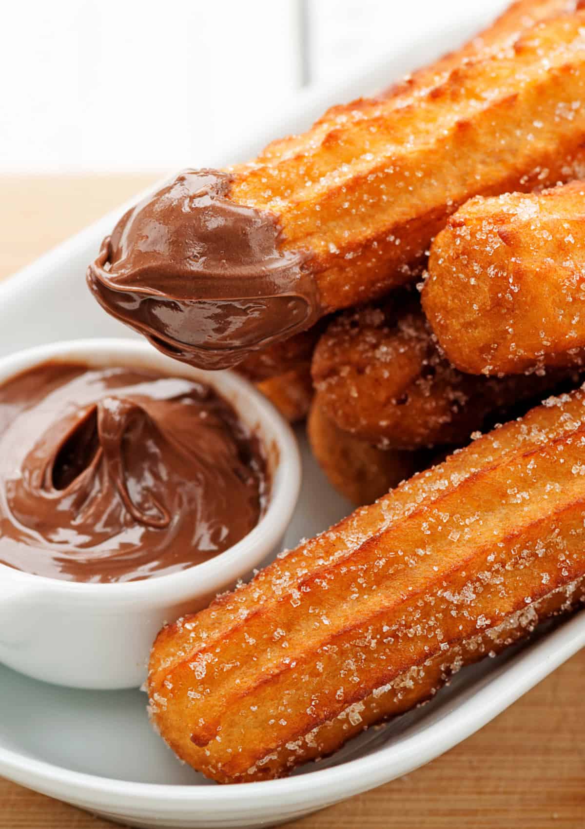 These Churros are soft on the inside, crisp and golden brown on the outside, and tossed with cinnamon sugar. A plate of churros, one dipped in chocolate
