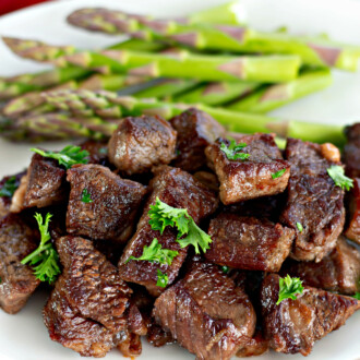 Garlic butter steak bites on a plate with roasted asparagus