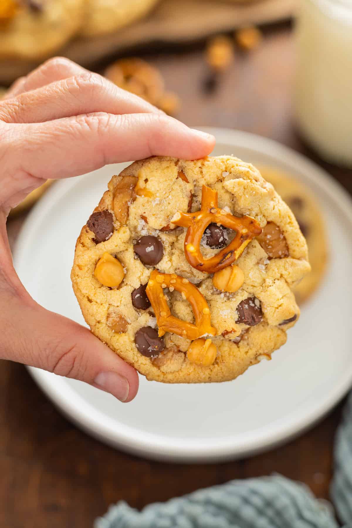 Made with brown butter, pretzels, caramel bits, and chocolate chips, Kitchen Sink Cookies are the perfect combination of sweet and salty. A hand holding a kitchen sink cookie