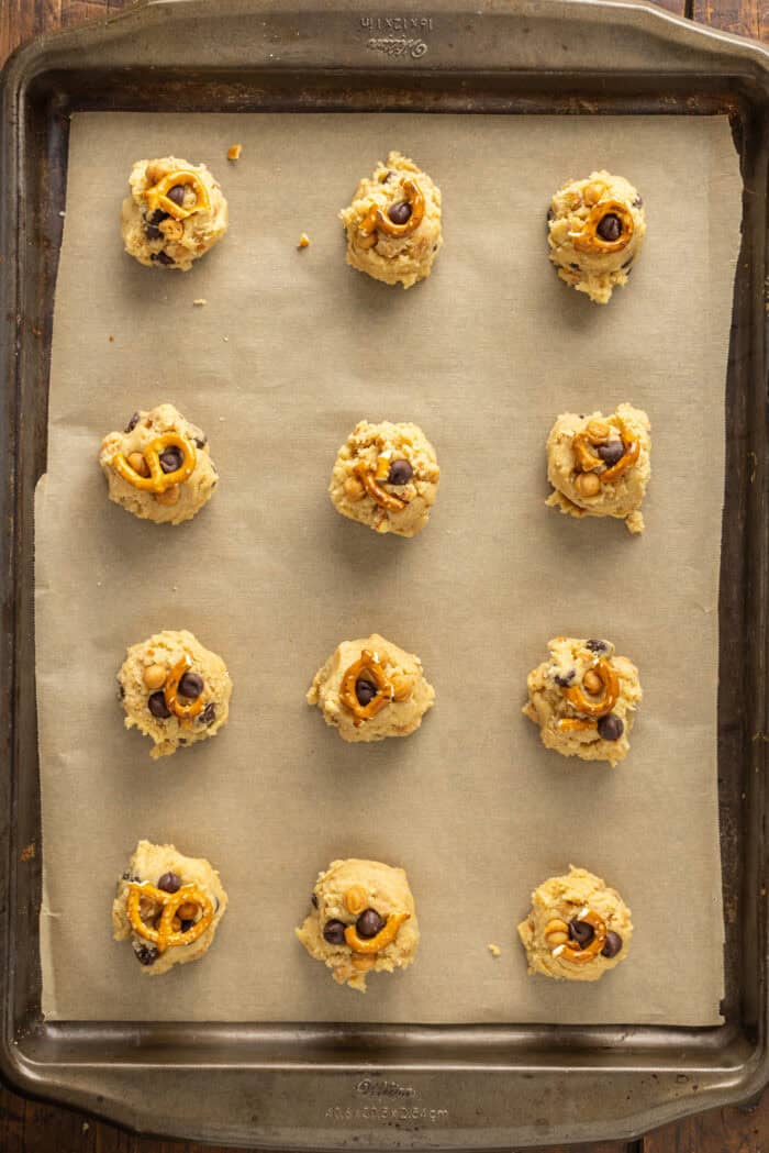 Made with brown butter, pretzels, caramel bits, and chocolate chips, Kitchen Sink Cookies are the perfect combination of sweet and salty. Large balls of cookie dough on a baking sheet