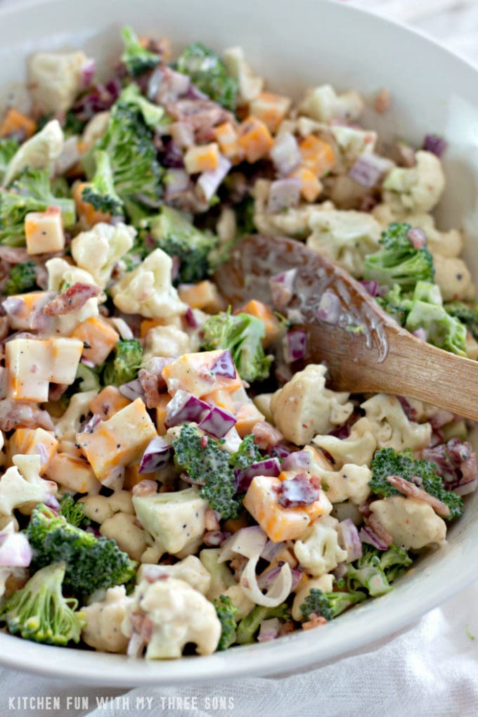 Tossing Low Carb Broccoli Salad in a large mixing bowl with a wooden spoon