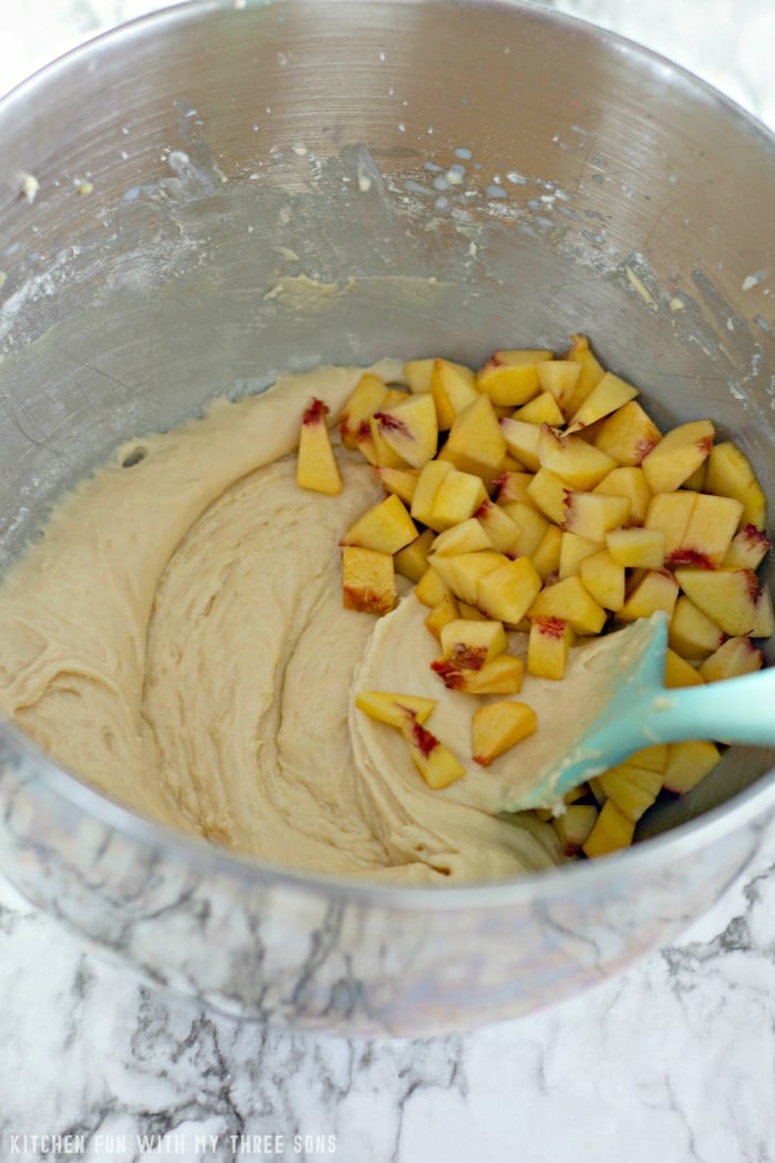 Sliced peaches being folded into the cake batter with a rubber spatula