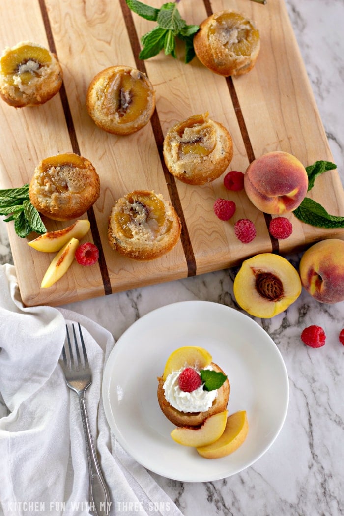 A mini peach cake on a plate with fresh peaches and more cakes on a serving platter beside it