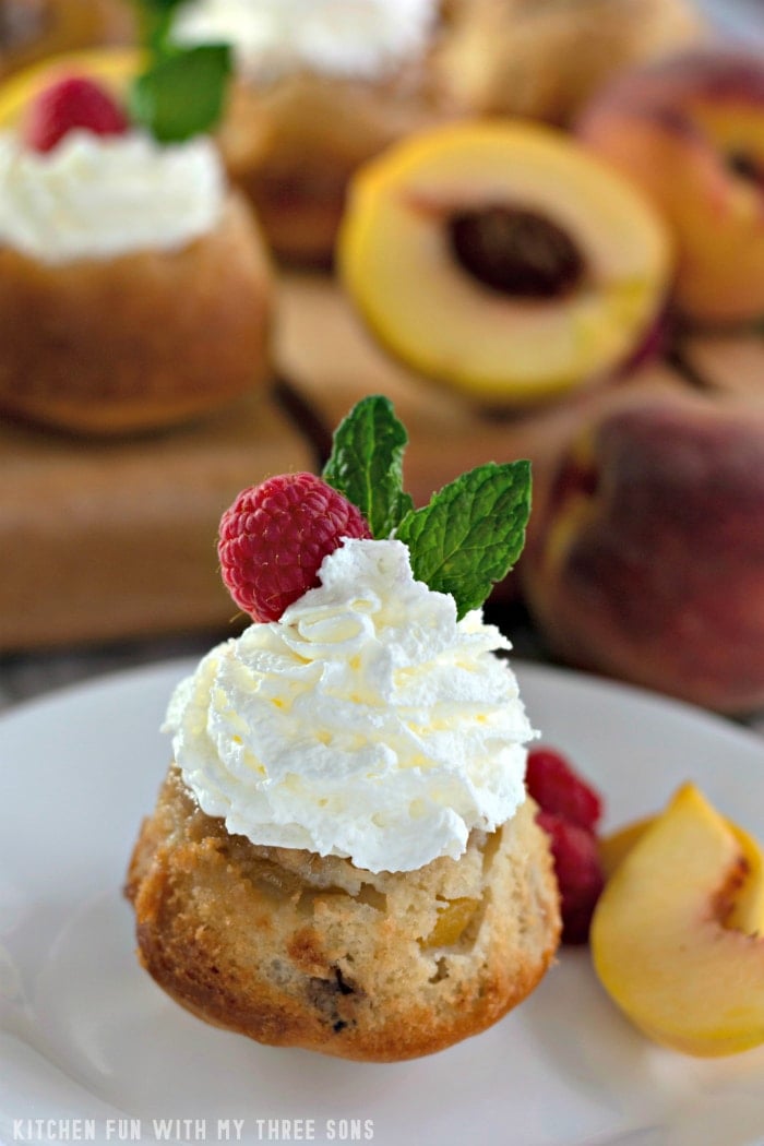 A mini peach upside down cake on a plate with fresh peaches and more mini cakes in the background
