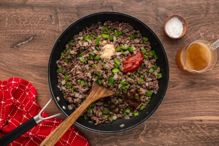 Philly Cheesesteak Sloppy Joes transform the cheesy goodness of a classic cheesesteak into a quick and easy sloppy joe in just 30 minutes. Ketchup and seasonings being stirred into cooked ground beef, peppers, and onions