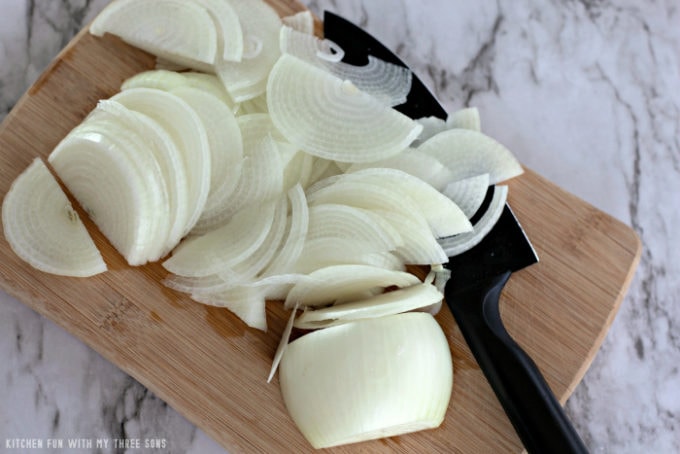 thinly sliced onions on a bamboo cutting board with a black knife