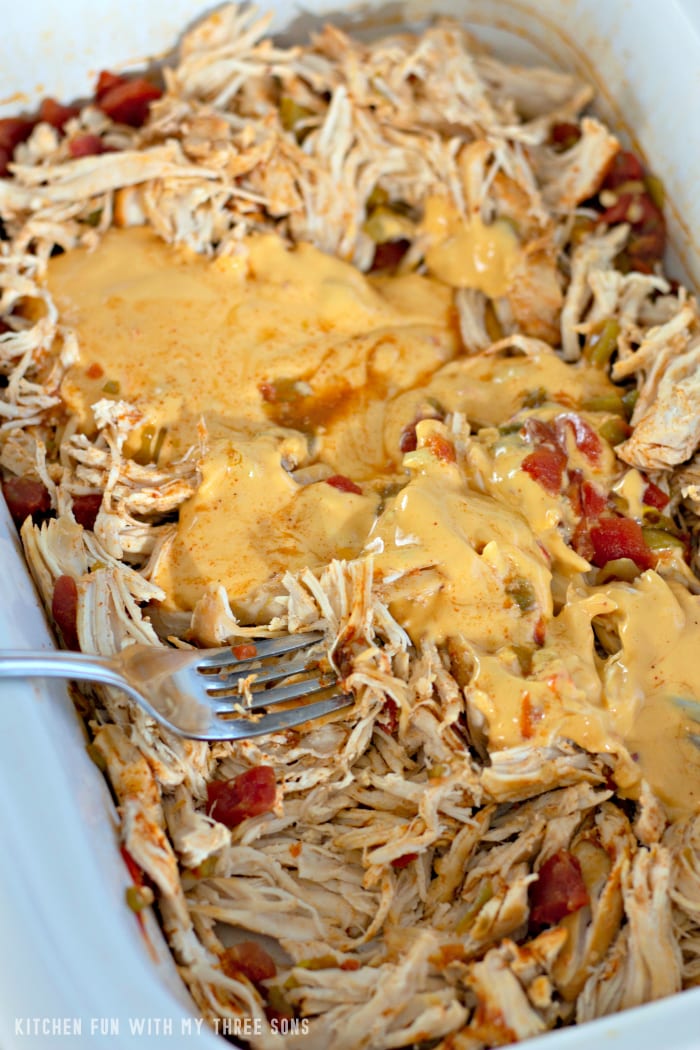 Shredded chicken inside of a slow cooker with queso poured on top