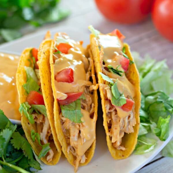 Three crock pot chicken tacos on a plate with fresh greens beside them