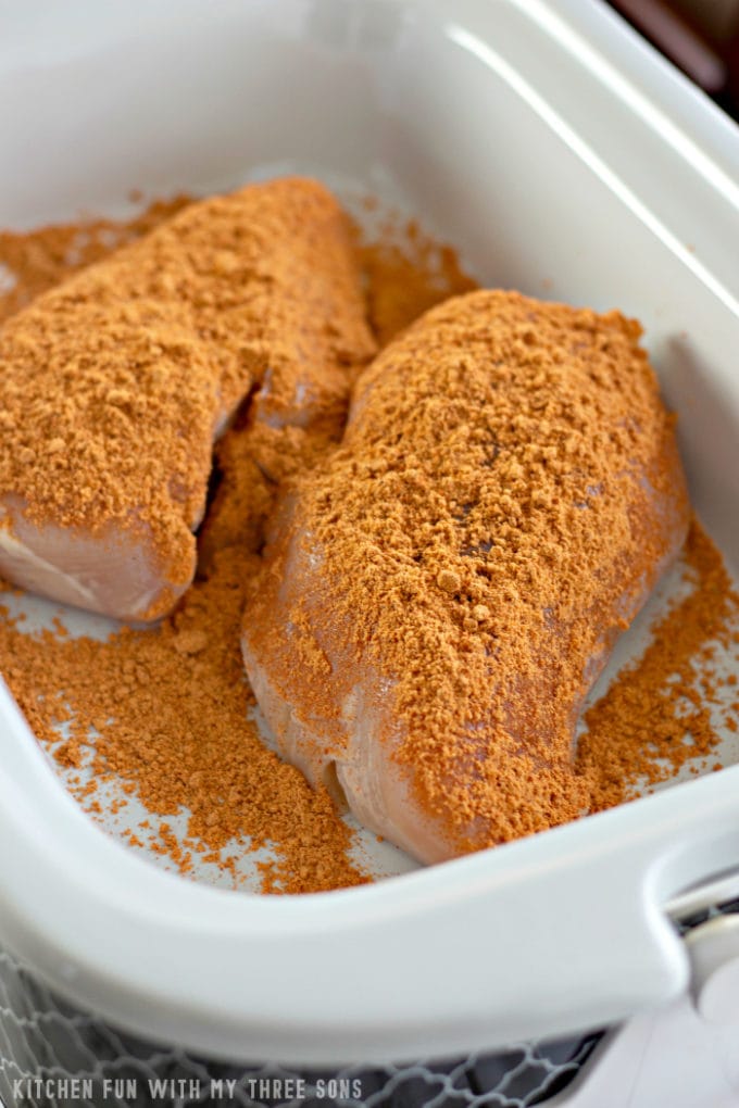 topping chicken with taco seasoning in a white slow cooker