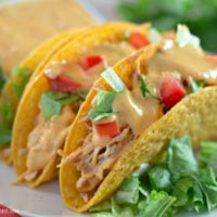 A close-up shot of three queso chicken tacos on a white serving plate