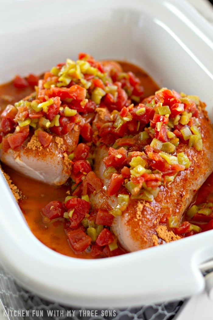 Raw chicken breasts in a large container with seasonings, diced green chiles and Rotel