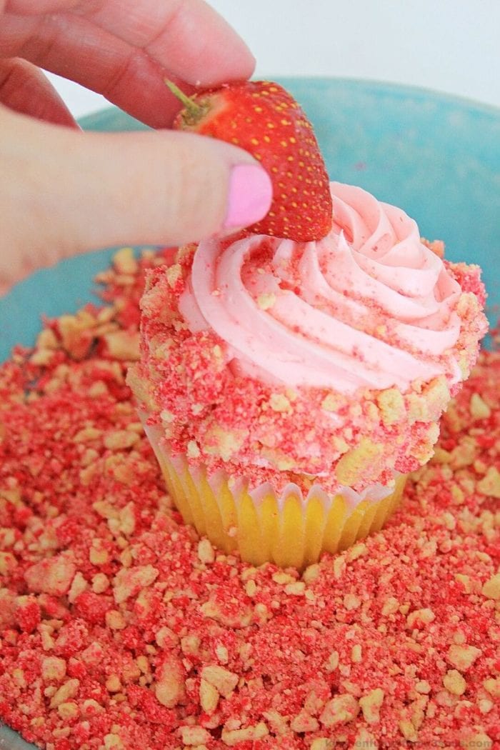 adding a strawberry to the top of a cupcake