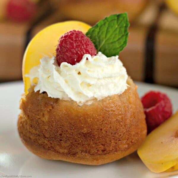 An upside-down peach cupcake on a dessert plate with whipped cream and fresh fruit on top
