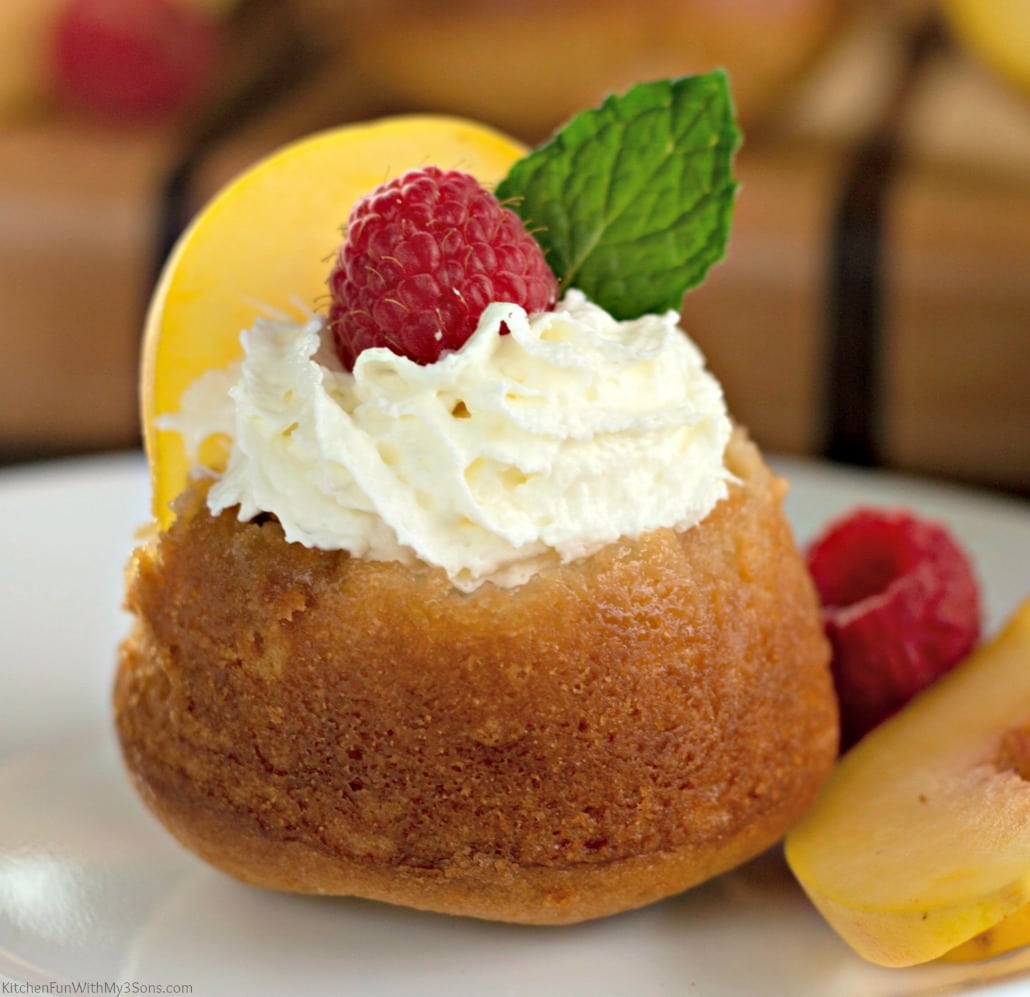 An upside-down peach cupcake on a dessert plate with whipped cream and fresh fruit on top