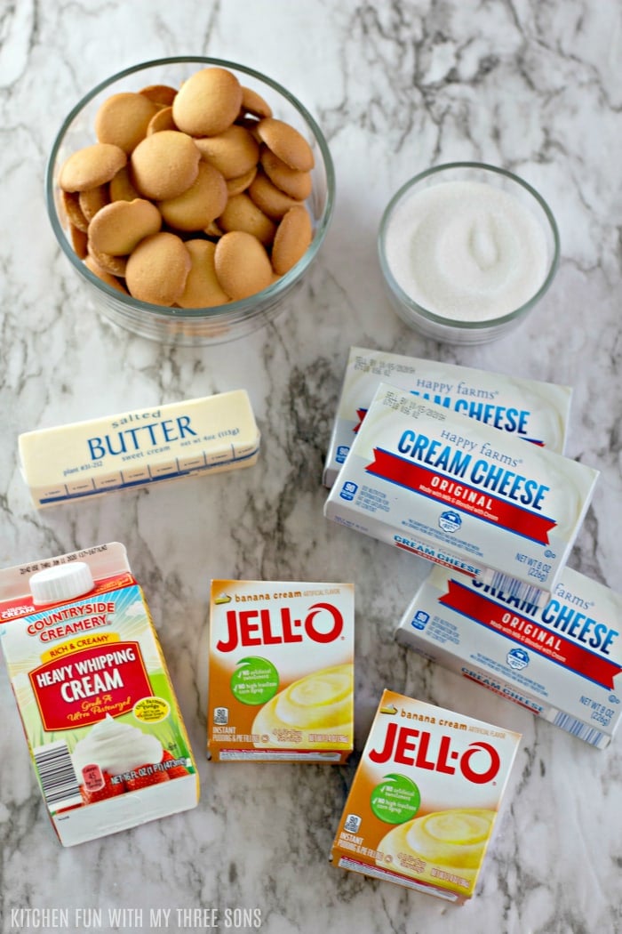 Nilla Wafers, a bowl of sugar, a stick of butter, three boxes of cream cheese, two jell-o packs and a carton of whipping cream all laid out on the counter.
