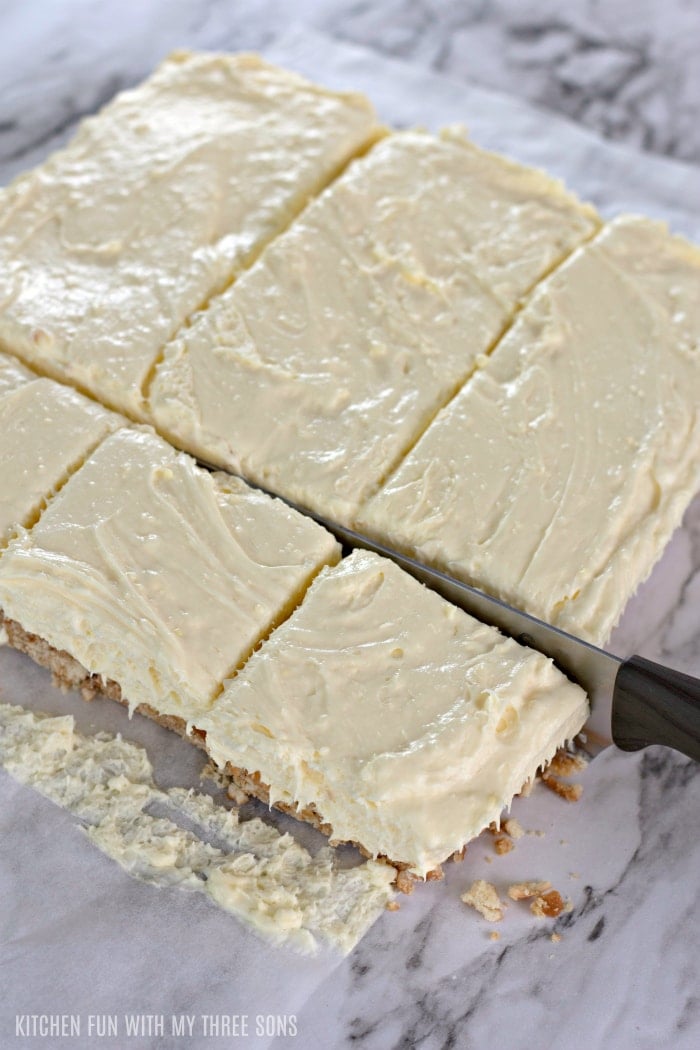 Someone slicing banana cream cheesecake into squares.