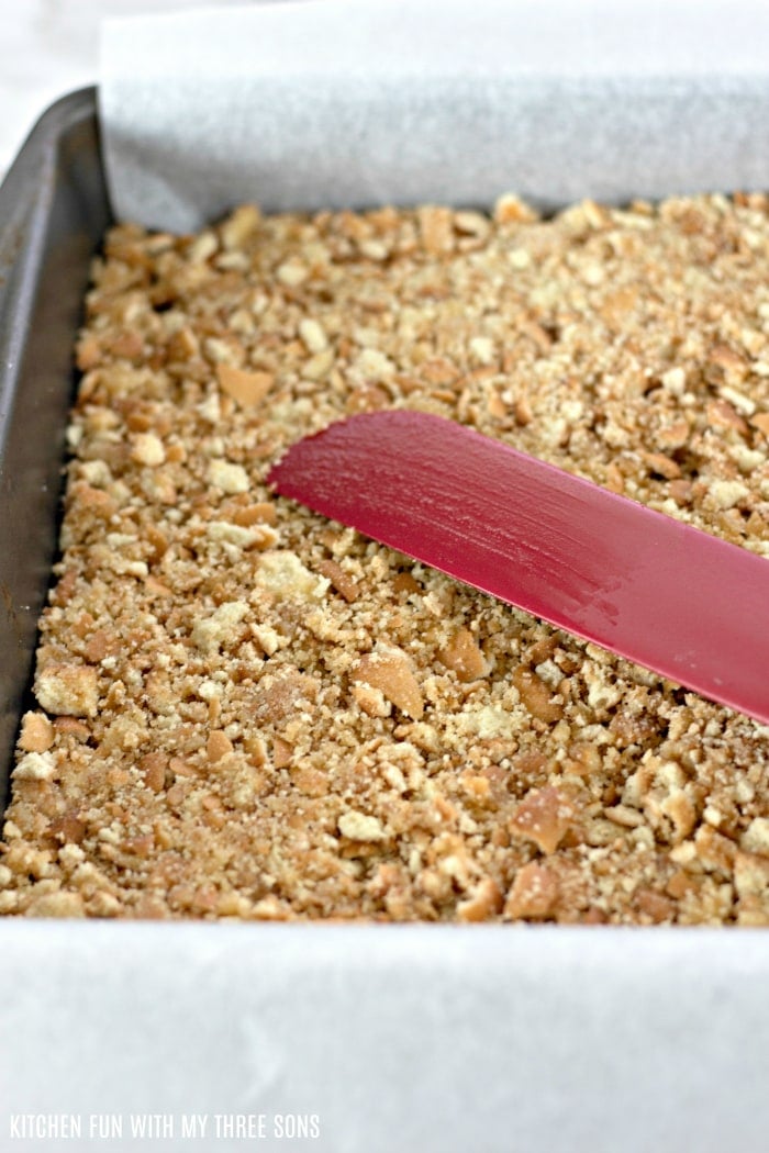Graham cracker crust being spread across a pan covered in parchment paper.