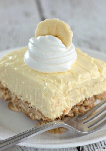 A single square of banana cream cheesecake topped with whipped cream and a banana slice.
