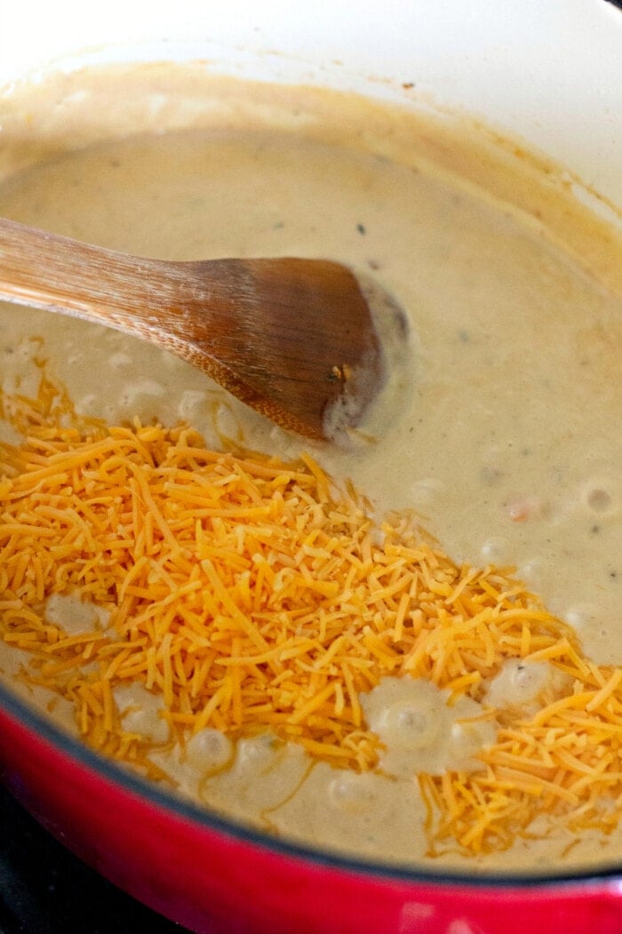 A wooden spoon stirring shredded cheese into beer cheese soup