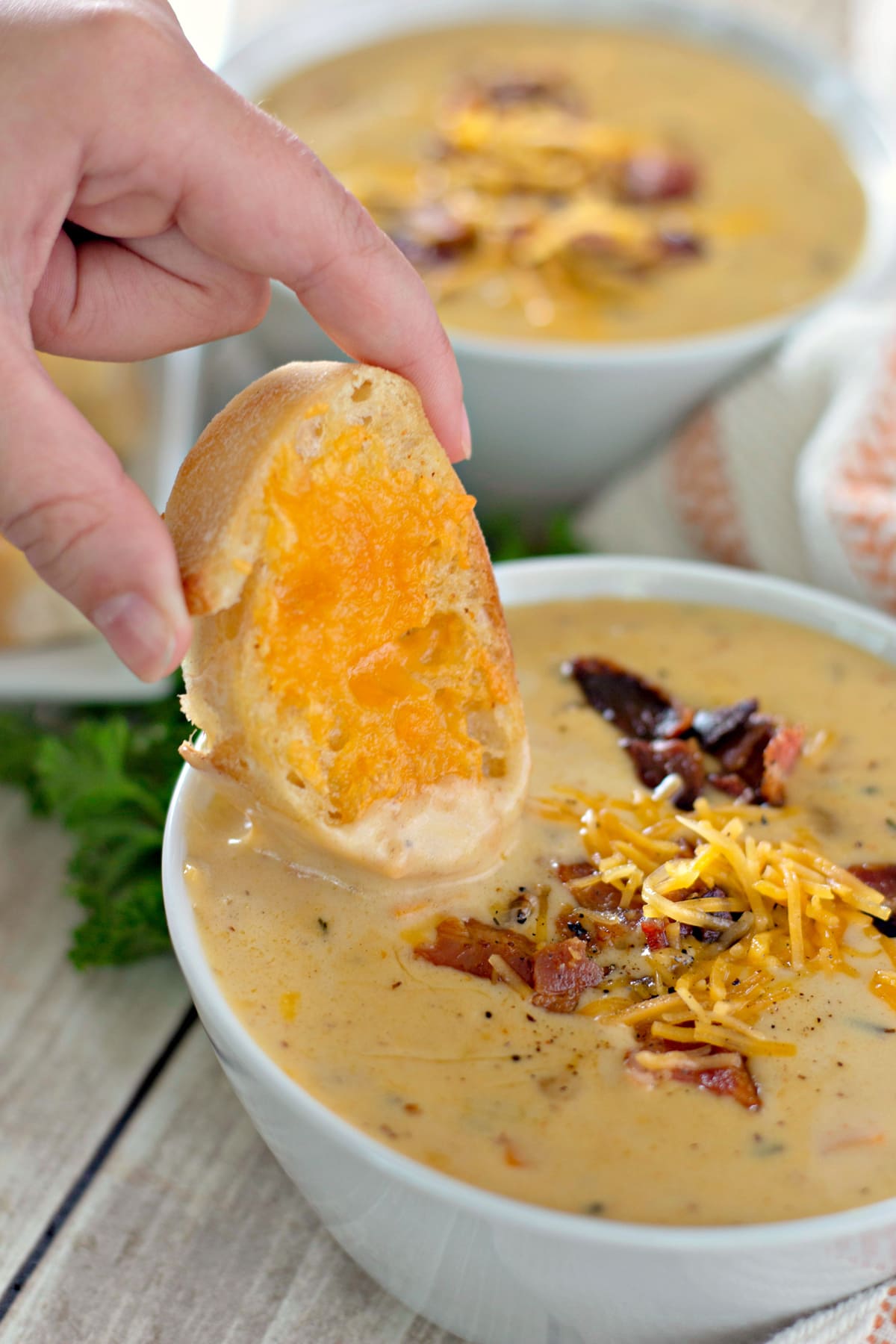 A hand dipping garlic cheese toast into a bowl of beer cheese soup