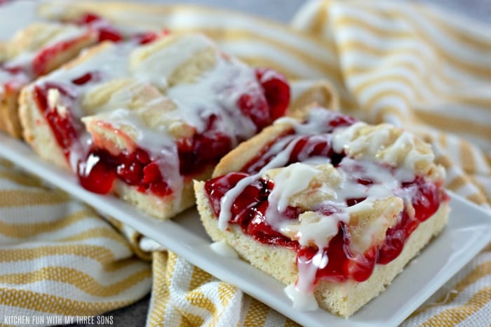 Two Cherry Pie Bars with gooey cherry filling drizzled with frosting on a plate.