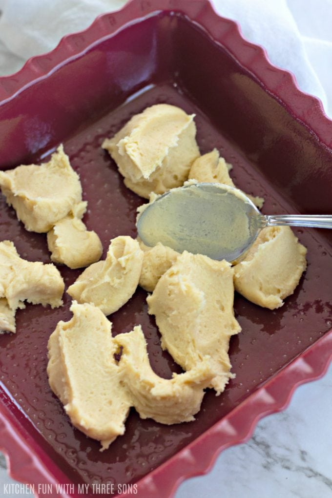 Sugar cookie dough being smoothed across the bottom of the pan with a spoon.