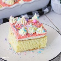 A slice of frosted Homemade Yellow Cake on a white plate, decorated with piped frosting swirls and rainbow sprinkles.