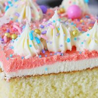 Close up of a slice of frosted Homemade Yellow Cake decorated with piped frosting swirls and rainbow sprinkles.