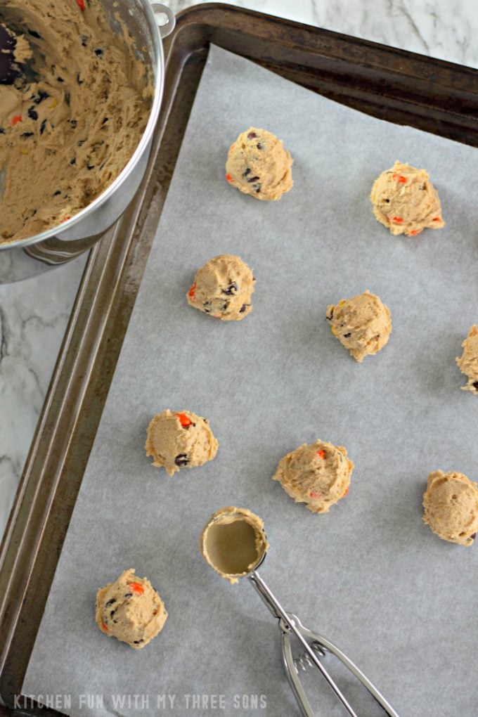scooping cookie dough onto a parchment paper lined baking sheet with a cookie scoop