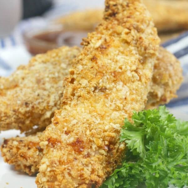 Air fryer pretzel crusted chicken tenders on a white plate next to a garnish of greens.
