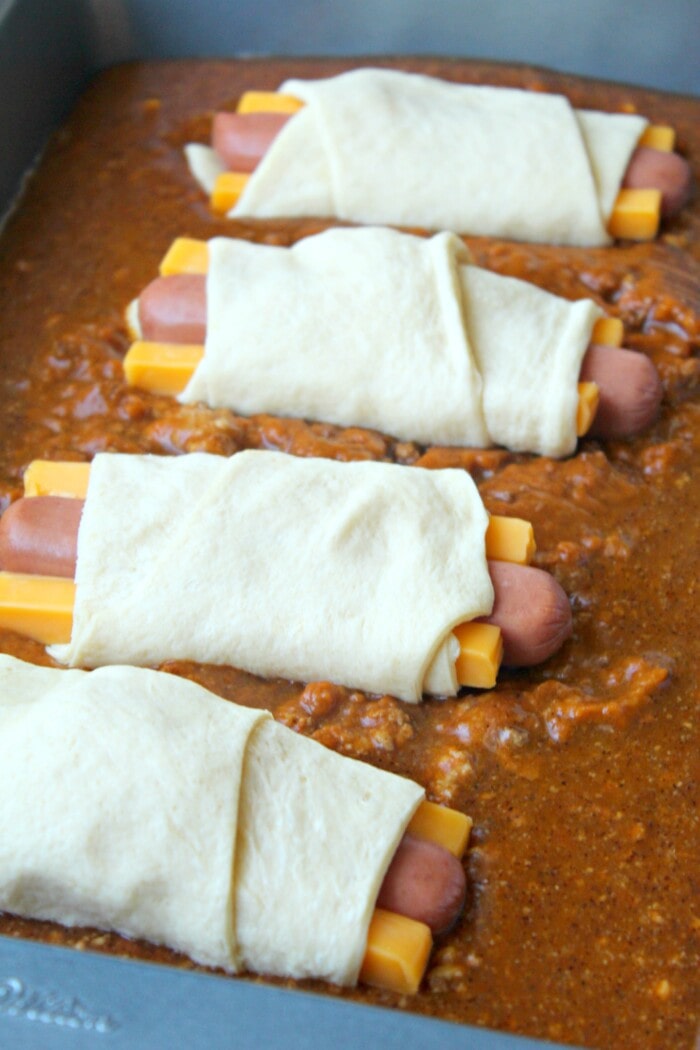 hot dogs wrapped in pizza dough and cheese laying on chili