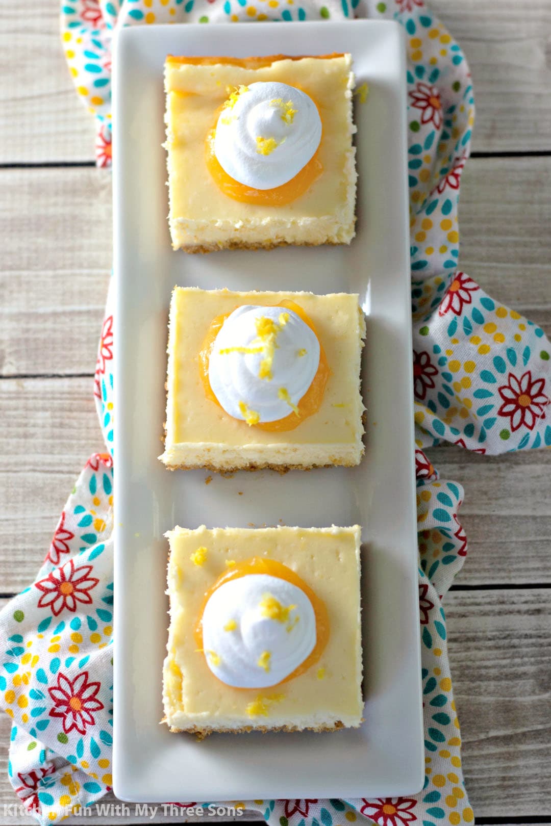 Easy Lemon Cheesecake Bars on a white platter with a flower print napkin