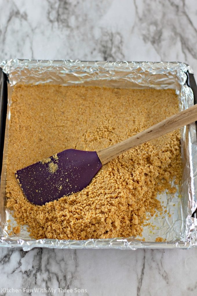 pressing graham crackers into a square pan lined with foil