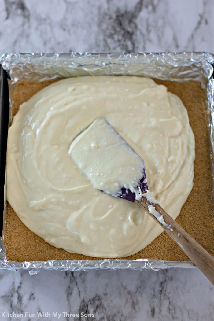 Spreading the cheesecake filling over the graham cracker crust in a foil lined baking pan