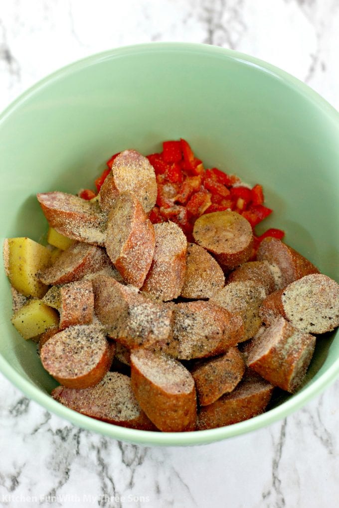 mixing kielbasa and potatoes and peppers with seasoning and olive oil in a mint green bowl