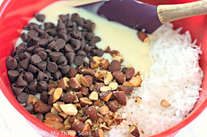 stirring together chocolate chips, sweetened condensed milk, coconut, and almonds in a red bowl