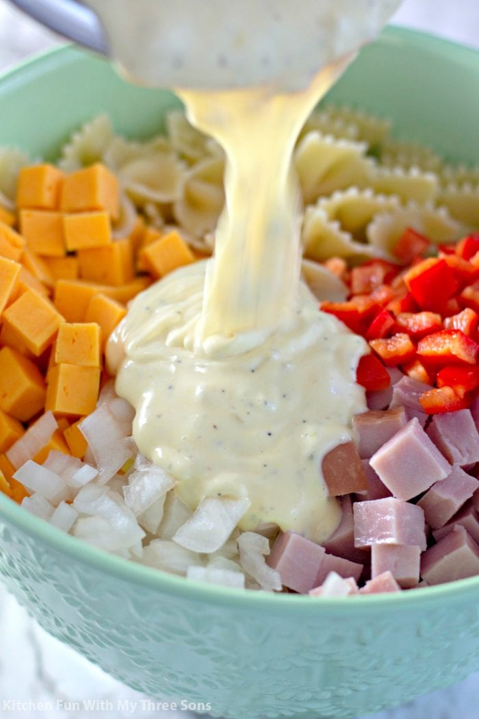 Mayonnaise dressing poured over bow tie pasta salad.