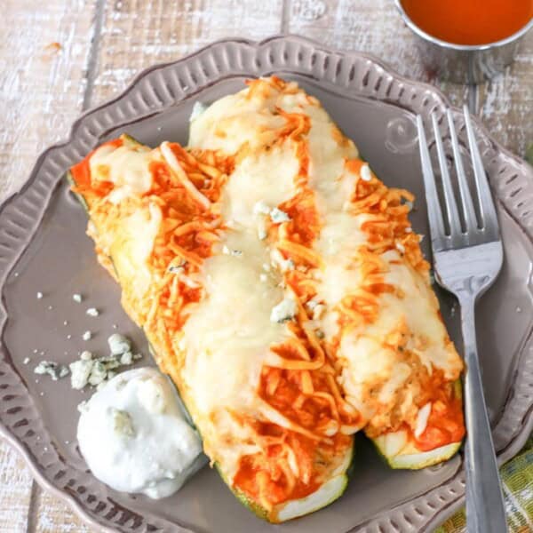 Overhead view of two buffalo chicken zucchini boats on a plate next to a fork and wing sauce.
