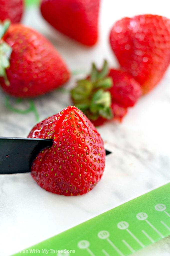 cutting strawberries on a cutting mat with a black paring knife