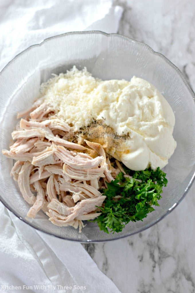 mixing together chicken, ricotta, Parmesan cheese, fresh parsley, and seasonings in a clear bowl