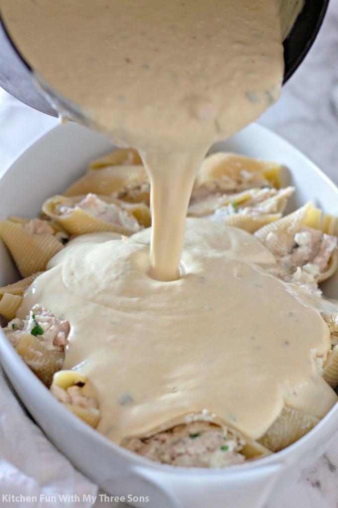 pouring a cheesy sauce over the chicken stuffed pasta shells