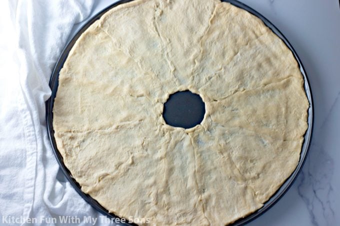 pressing crescent rolls into a ring on a pizza pan
