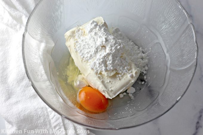 cream cheese, powdered sugar, and an egg in a clear bowl